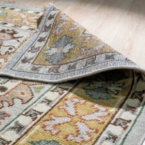 A dense, multicolored floral and geometric rug is partially rolled on blonde wood flooring.