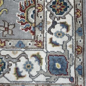 Detail of a traditional patterned rug border with gray, cream, blue, red, and yellow floral motifs.