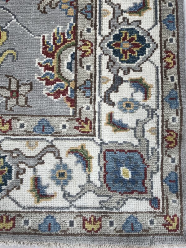 Detail of a traditional patterned rug border with gray, cream, blue, red, and yellow floral motifs.