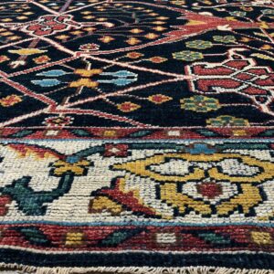 Detailed dark rug with colorful geometric patterns in red, gold, and blue, visible on light flooring.