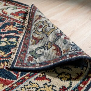 Navy and red patterned rug folded over, showing its tightly woven back against light wood flooring.