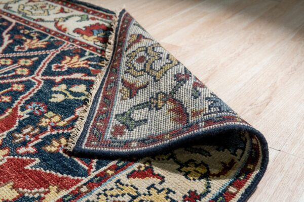Navy and red patterned rug folded over, showing its tightly woven back against light wood flooring.