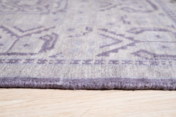 Plush gray and purple rug edge with tribal pattern details shown on light wood planks.