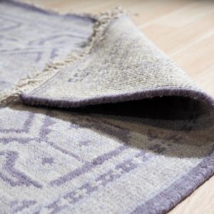 Close-up of a low-pile rug with a purple geometric pattern rolled on light wood floor.