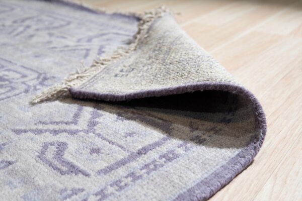 Close-up of a low-pile rug with a purple geometric pattern rolled on light wood floor.