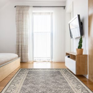 Beige and dark gray traditional rug anchors a bright room with light wood floors and sheer window curtains.