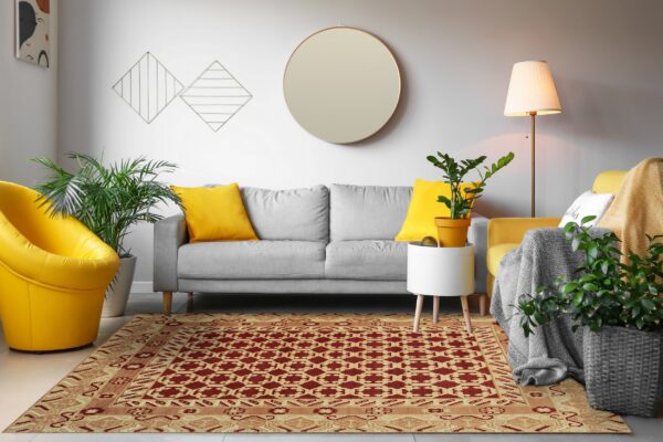 A geometric red and tan pattern area rug sits on light flooring under a gray sofa and yellow accent chairs.