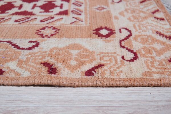 High-pile rug featuring stylized red and tan geometric patterns rests on white-washed wooden planks.