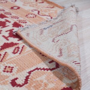A red and peach tribal-patterned rug is folded over, showing its woven backing on light wood flooring.