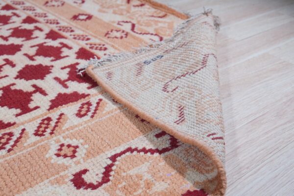 A red and peach tribal-patterned rug is folded over, showing its woven backing on light wood flooring.