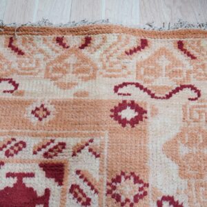 Textured rug featuring cream, peach, and burgundy geometric patterns, resting on light wood plank flooring.