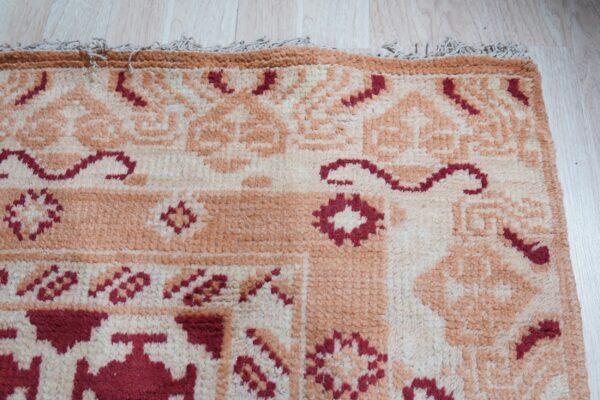 Textured rug featuring cream, peach, and burgundy geometric patterns, resting on light wood plank flooring.