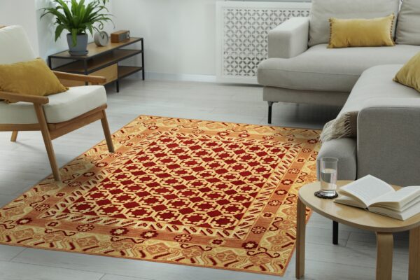 Traditional rug in red and golden yellow with geometric patterns lies between a beige sofa and armchair.
