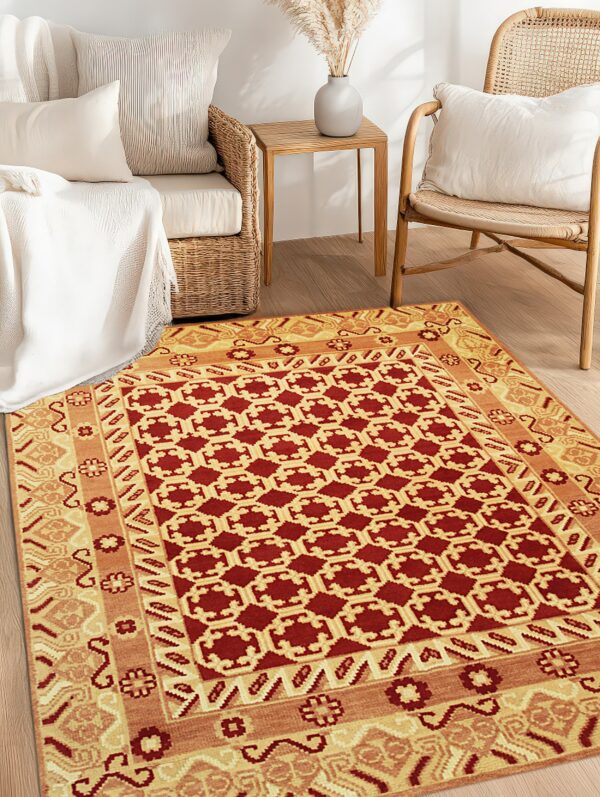 Red and gold geometric rug on wood floors between woven rattan sofa and chair.