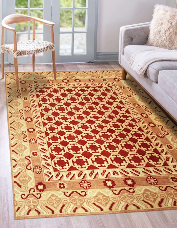 Red and gold geometric rug with multiple borders near a gray sofa and wooden chair on wood plank flooring.