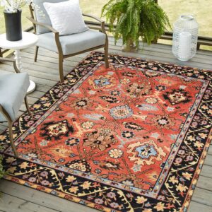 Terracotta traditional rug with black border and floral motifs beneath gray chairs on a wooden deck.