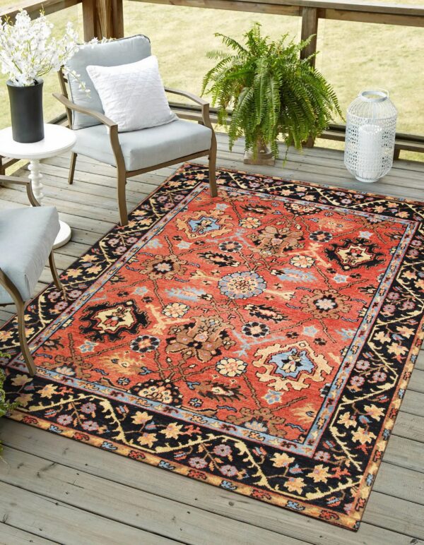 Terracotta traditional rug with black border and floral motifs beneath gray chairs on a wooden deck.