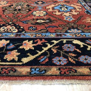 Rust-colored rug with complex traditional designs in navy, blue, and tan on light wood floors.
