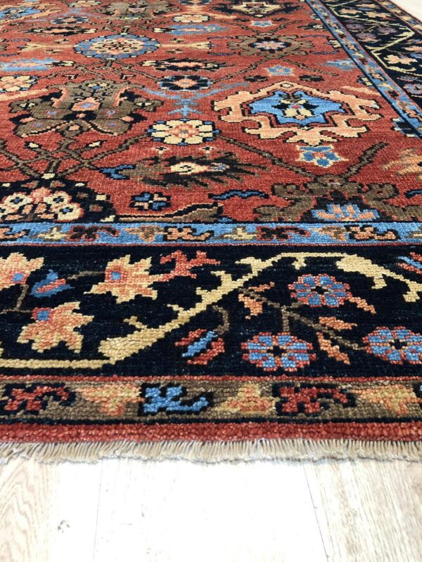 Rust-colored rug with complex traditional designs in navy, blue, and tan on light wood floors.