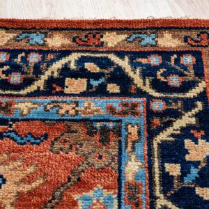 Corner detail of a patterned rug with navy, rust, beige, and blue accents on light wood flooring.
