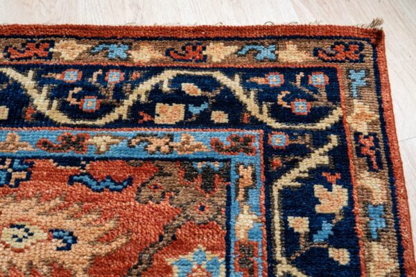 Corner detail of a patterned rug with navy, rust, beige, and blue accents on light wood flooring.