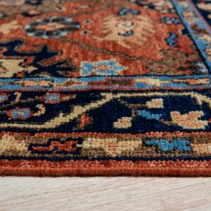 Close-up of a medium pile rug border in navy, rust, and beige, resting on light wood grain flooring.
