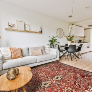 A deep red traditional patterned rug lies on light wood floors beneath a gray sofa and wood tables.