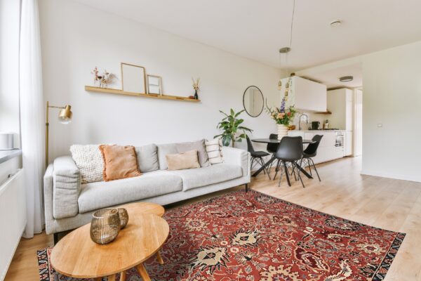 A deep red traditional patterned rug lies on light wood floors beneath a gray sofa and wood tables.