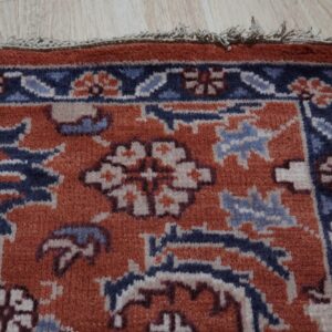 Low-pile rug in rust, navy, and light blue features a detailed traditional border on wood floors.