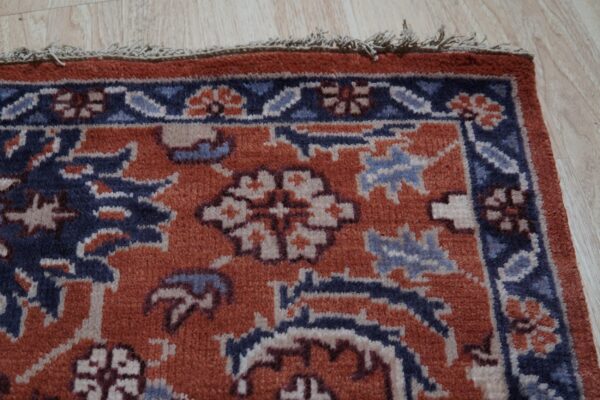 Low-pile rug in rust, navy, and light blue features a detailed traditional border on wood floors.