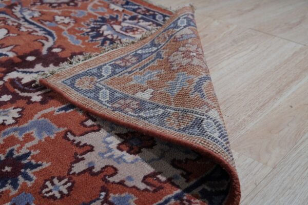 Close-up showing the ornate terracotta rug pile and the densely woven reverse side border on light flooring.