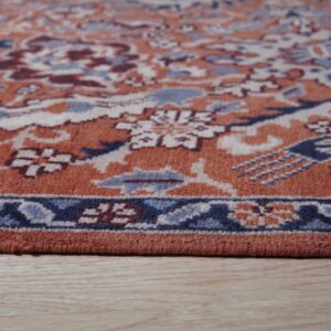 Close-up of the border of an orange and blue traditional rug placed on light wooden floor.