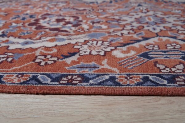 Close-up of the border of an orange and blue traditional rug placed on light wooden floor.