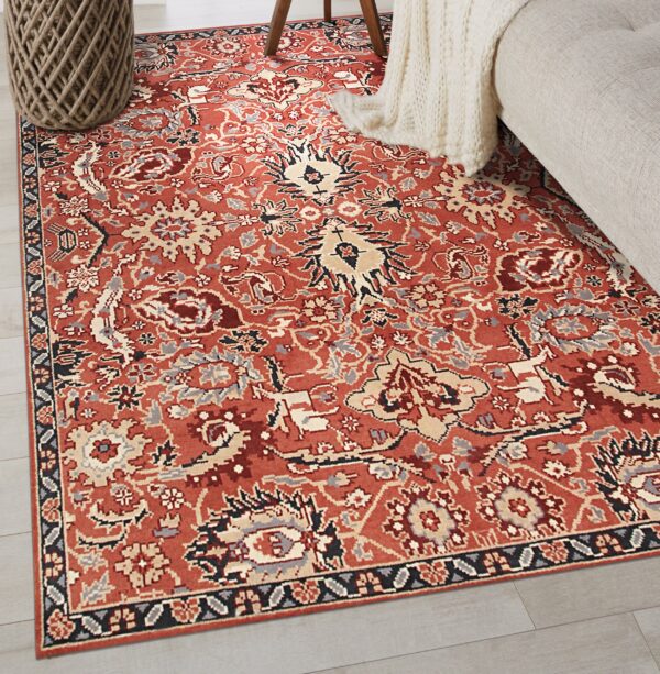 A rust-colored traditional rug with complex patterns in beige, gray, and black rests on light gray floors.