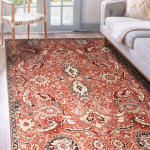 Rust and beige traditional patterned rug on wood flooring in a living room with a chair and sofa.