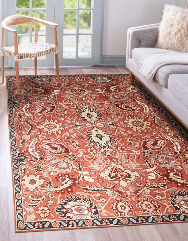 Rust and beige traditional patterned rug on wood flooring in a living room with a chair and sofa.