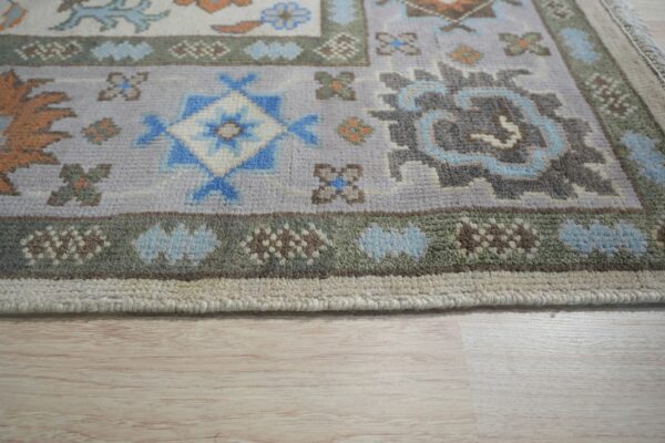 Geometric rug detail showing gray, blue, terracotta, and olive borders rests on light wood floor.