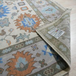 Traditional rug with blue and orange motifs, showing fringe and woven backing on light wood floors.