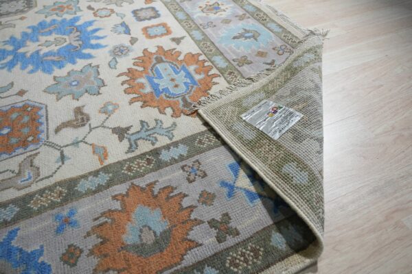 Traditional rug with blue and orange motifs, showing fringe and woven backing on light wood floors.