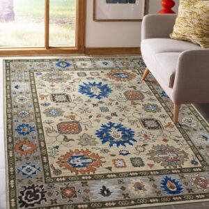 Beige and grey traditional rug with bold blue and terracotta motifs next to a cream chair and window.