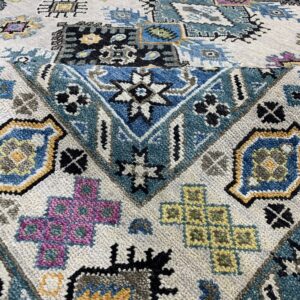 High-pile rug texture showing detailed geometric patterns in blue, pink, black, and mustard yellow on off-white.