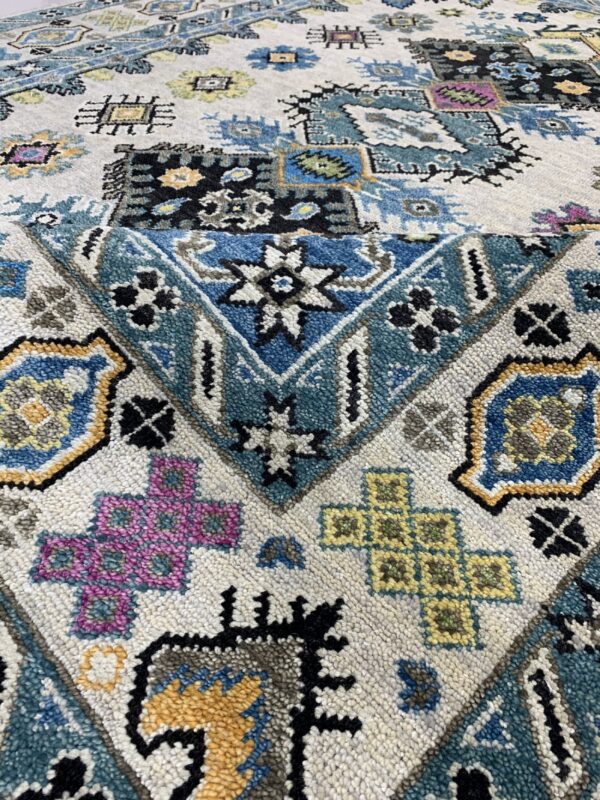 High-pile rug texture showing detailed geometric patterns in blue, pink, black, and mustard yellow on off-white.