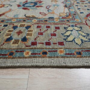 Medium pile gray rug featuring blue, red, and orange traditional patterns on light wood flooring.