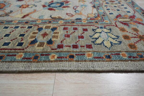 Medium pile gray rug featuring blue, red, and orange traditional patterns on light wood flooring.