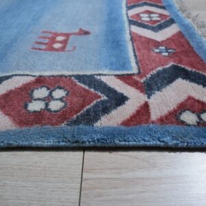 Medium-pile blue rug featuring a stylized animal and geometric borders rests on light wood plank flooring.