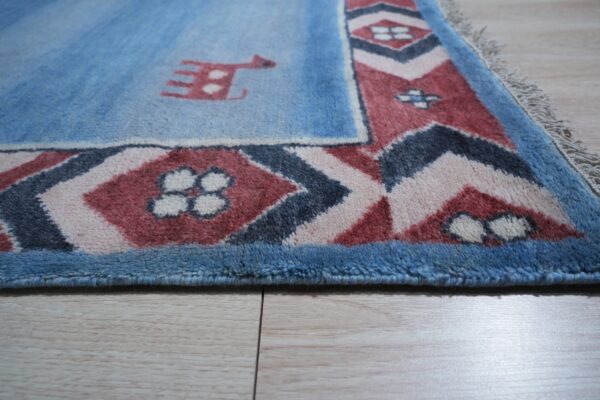 Medium-pile blue rug featuring a stylized animal and geometric borders rests on light wood plank flooring.