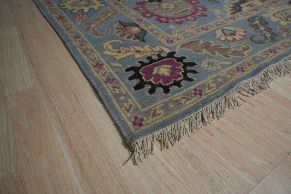 A traditional blue rug with yellow and magenta floral motifs rests on light blonde plank flooring.