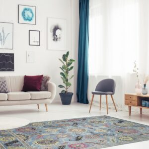 A light blue rug with a traditional medallion pattern anchors a brightly lit living room with a beige sofa and wooden furniture.