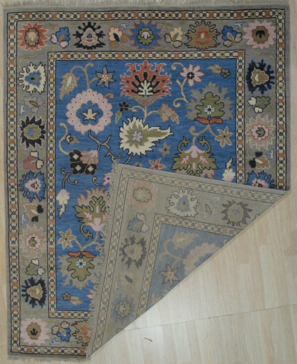 Blue floral rug with gray border on light wood flooring, showing the lighter patterned reverse side.