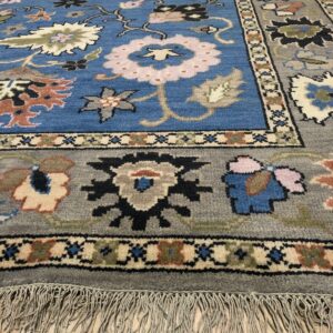 Traditional blue and gray floral patterned rug with long fringe rests on light wood flooring.